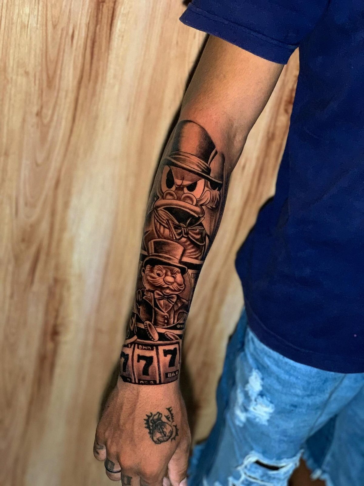 Tatuagem realista no antebraço e na mão com personagem de cartola, cédulas e caça-níquel