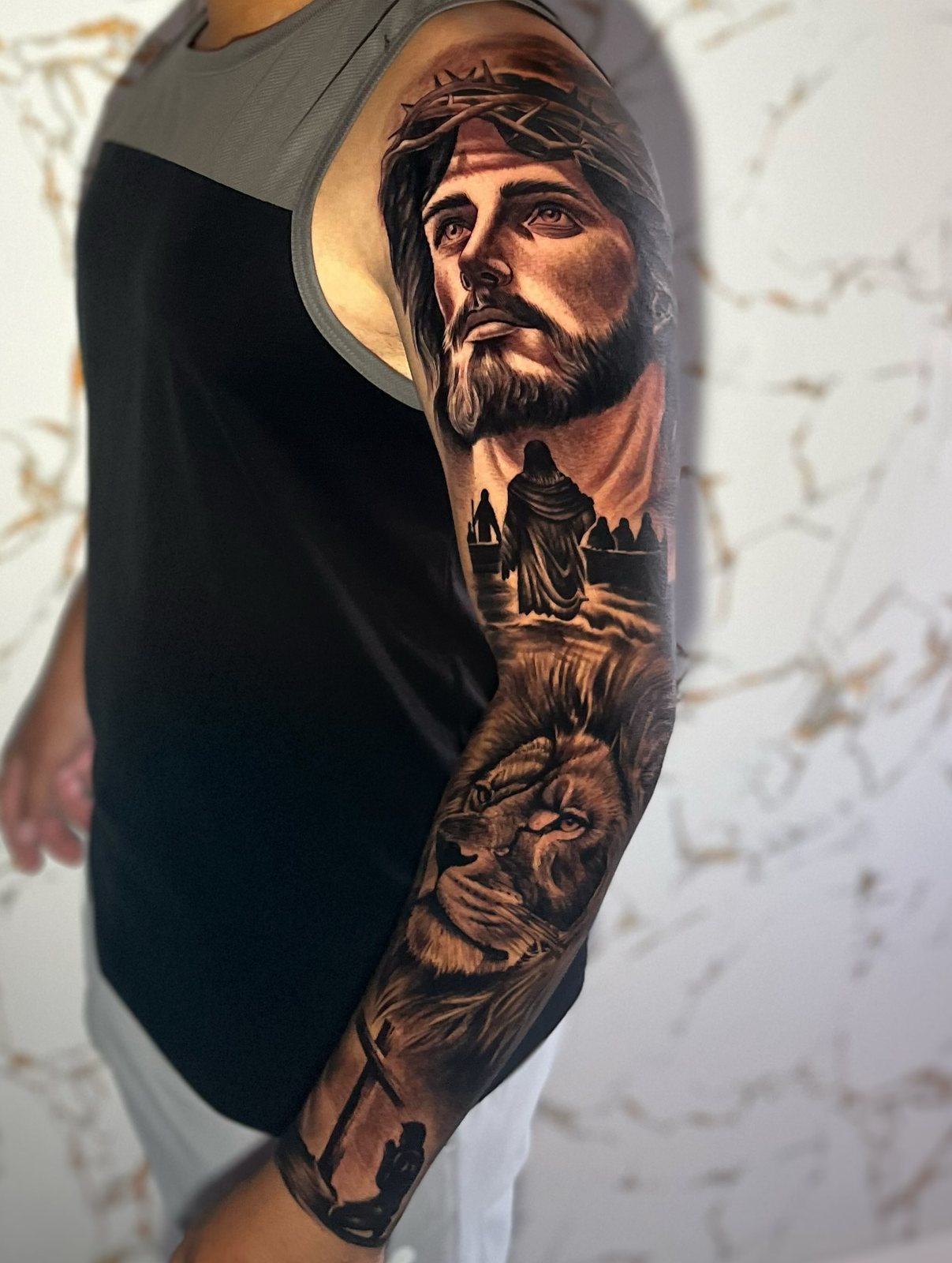Braço fechado em realismo preto e cinza: rosto de Jesus olhando para o alto, travessia e leão