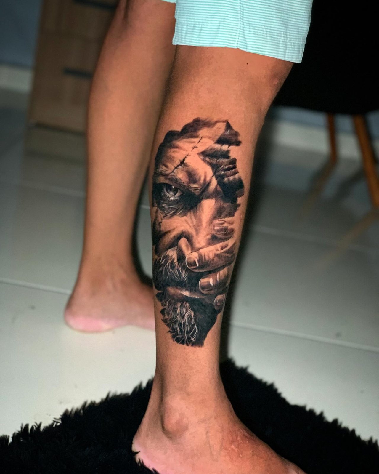 Tatuagem realista na panturrilha: rosto masculino envolto em fragmentos de pedra